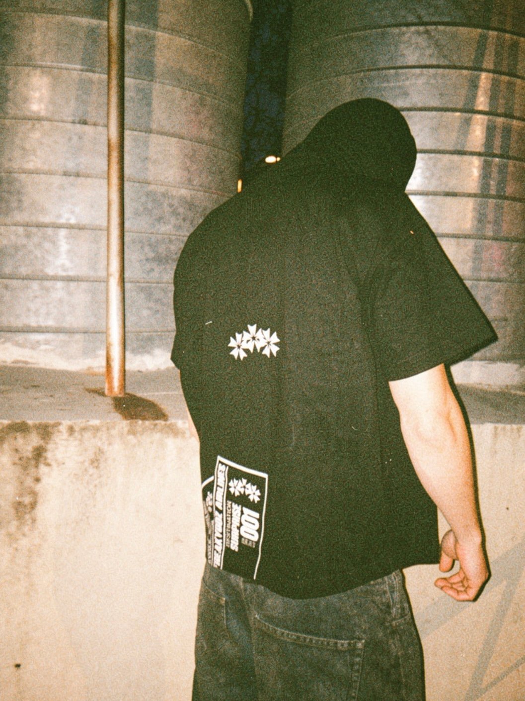 Espalda de la camiseta FREAKYDDZ con estampado de estrellas y etiqueta de equipaje numerada 001